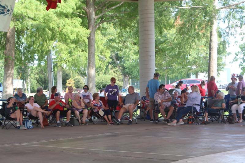 A group of people are sitting in chairs under a canopy in a park.