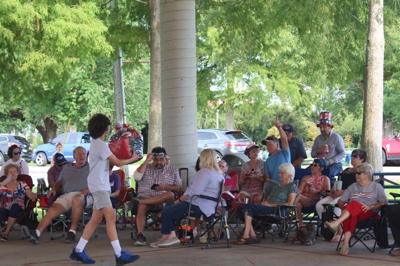 A group of people are sitting in chairs under a canopy in a park.