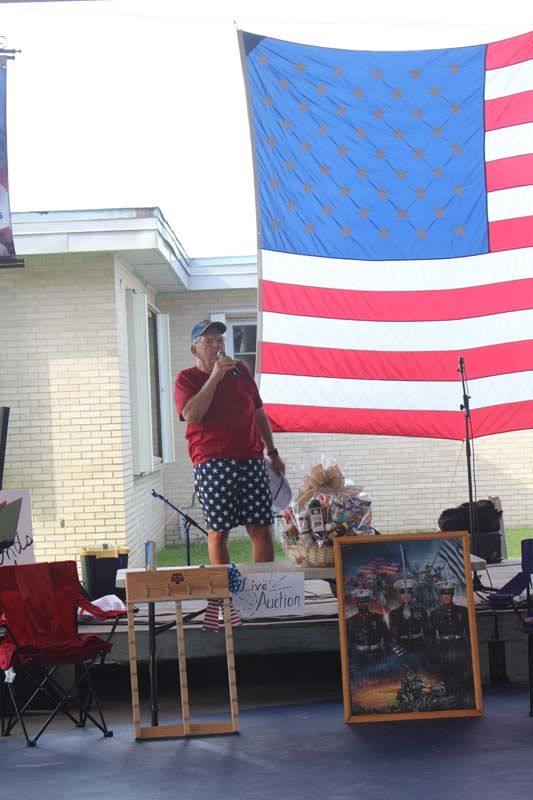 A man is standing in front of an american flag holding a microphone.