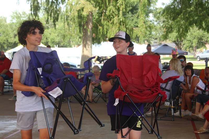 Two young boys are carrying folding chairs in a park.
