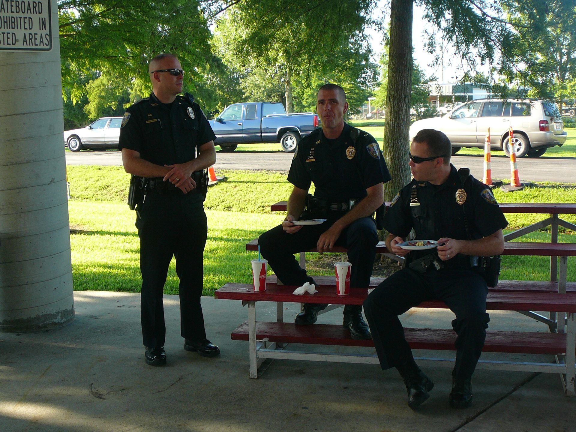 Three police officers sit at a picnic table in front of a no parking sign