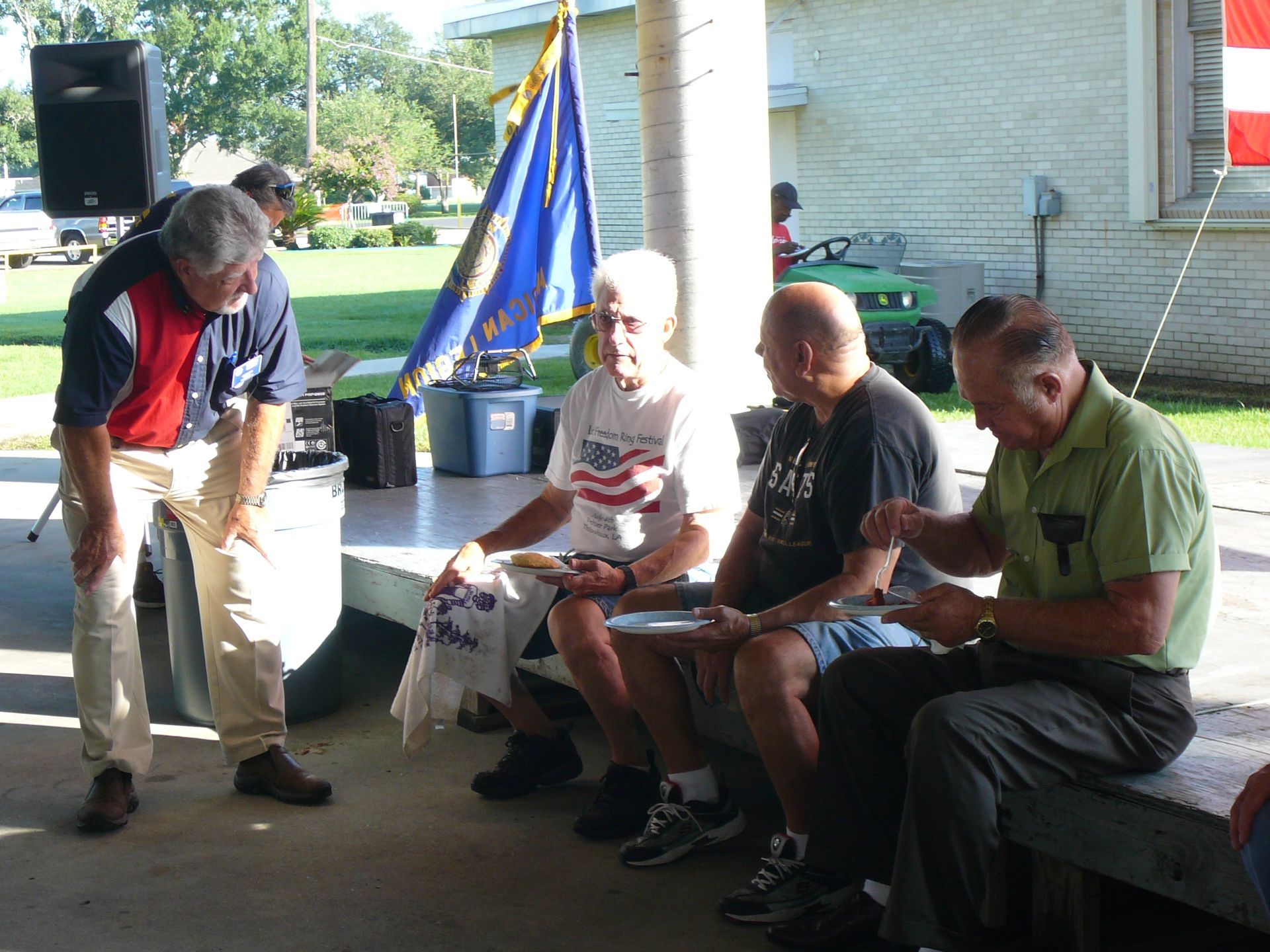 A group of men sit on a bench in front of a flag
