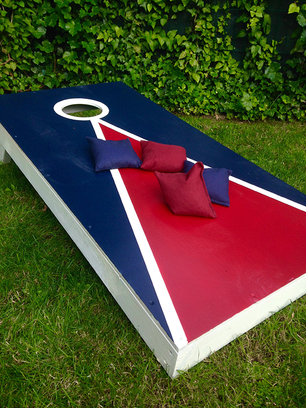 A red , white and blue cornhole board is sitting on top of a lush green field.