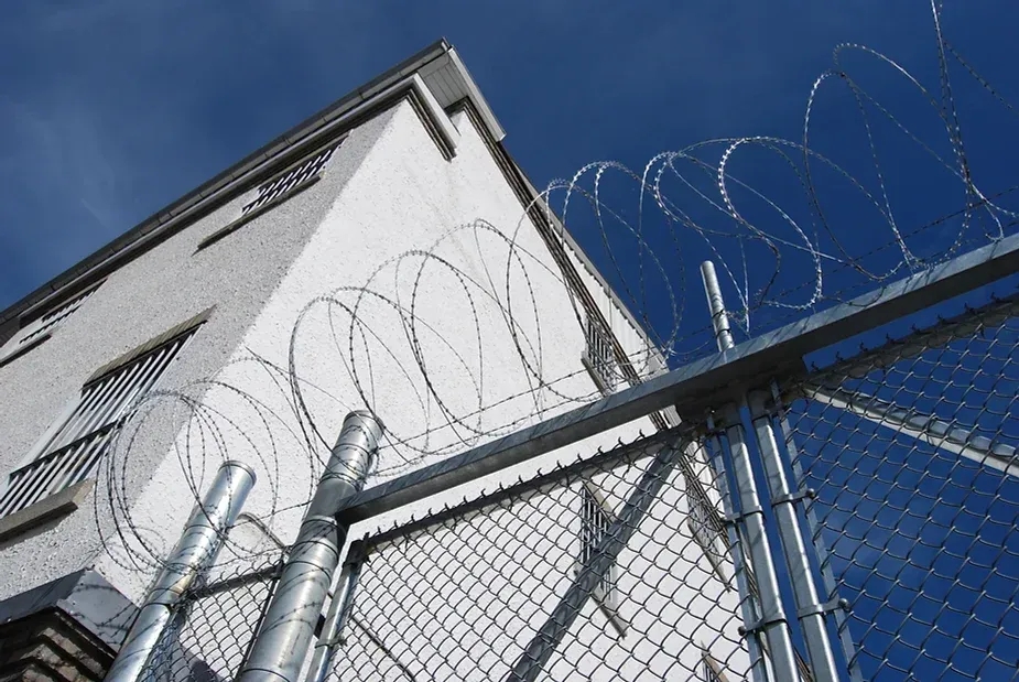 A barbed wire fence surrounds a building with a blue sky in the background