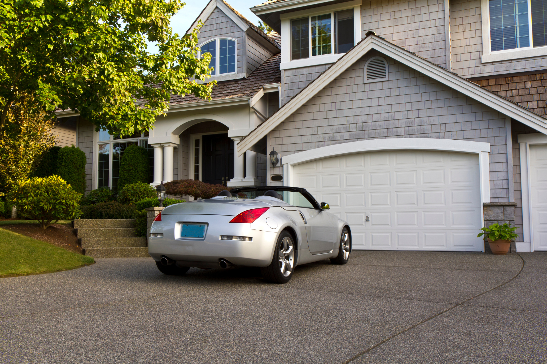 A silver car is parked in front of a large house.