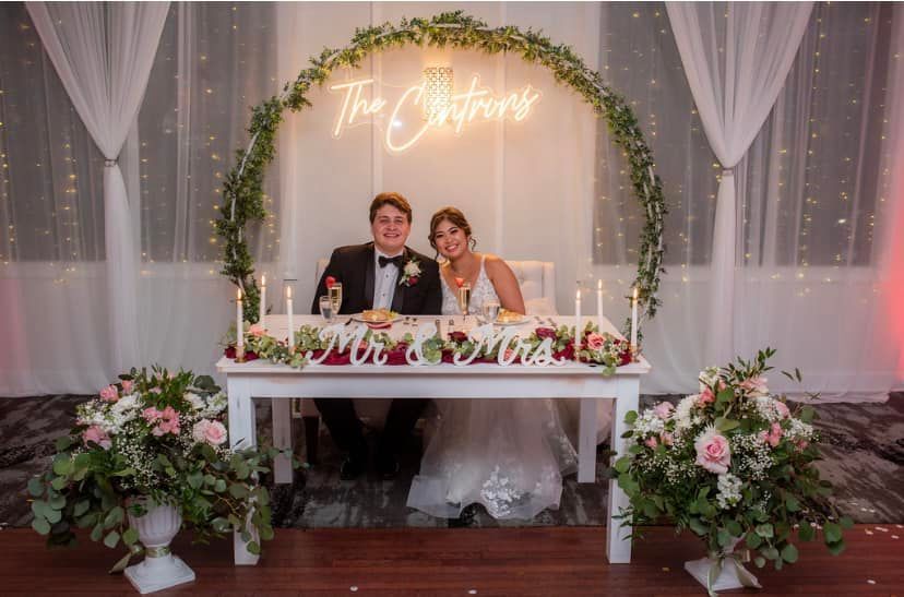 A bride and groom are sitting at a table in front of a neon sign