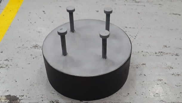 Un objeto metálico con tornillos sujetos está colocado sobre un suelo de hormigón.