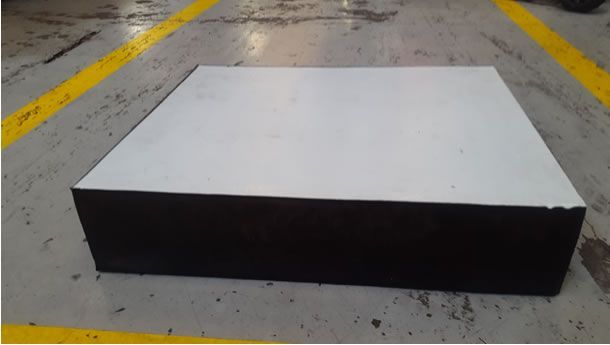 Una caja en blanco y negro está sobre un piso de concreto al lado de una línea amarilla.