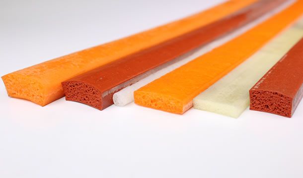 Cuatro palos de goma de diferentes colores están alineados sobre una superficie blanca.