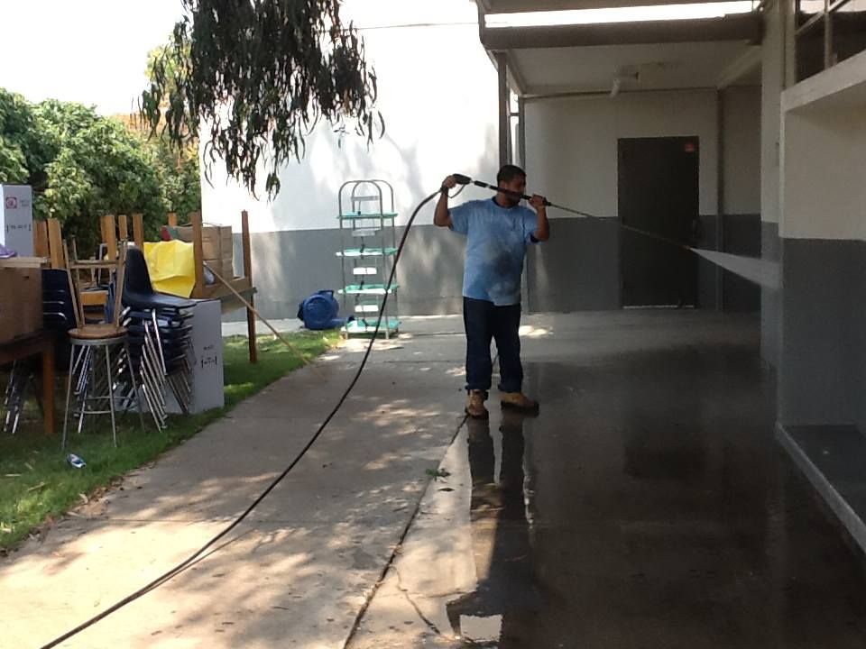 A man is using a high pressure hose to clean a sidewalk