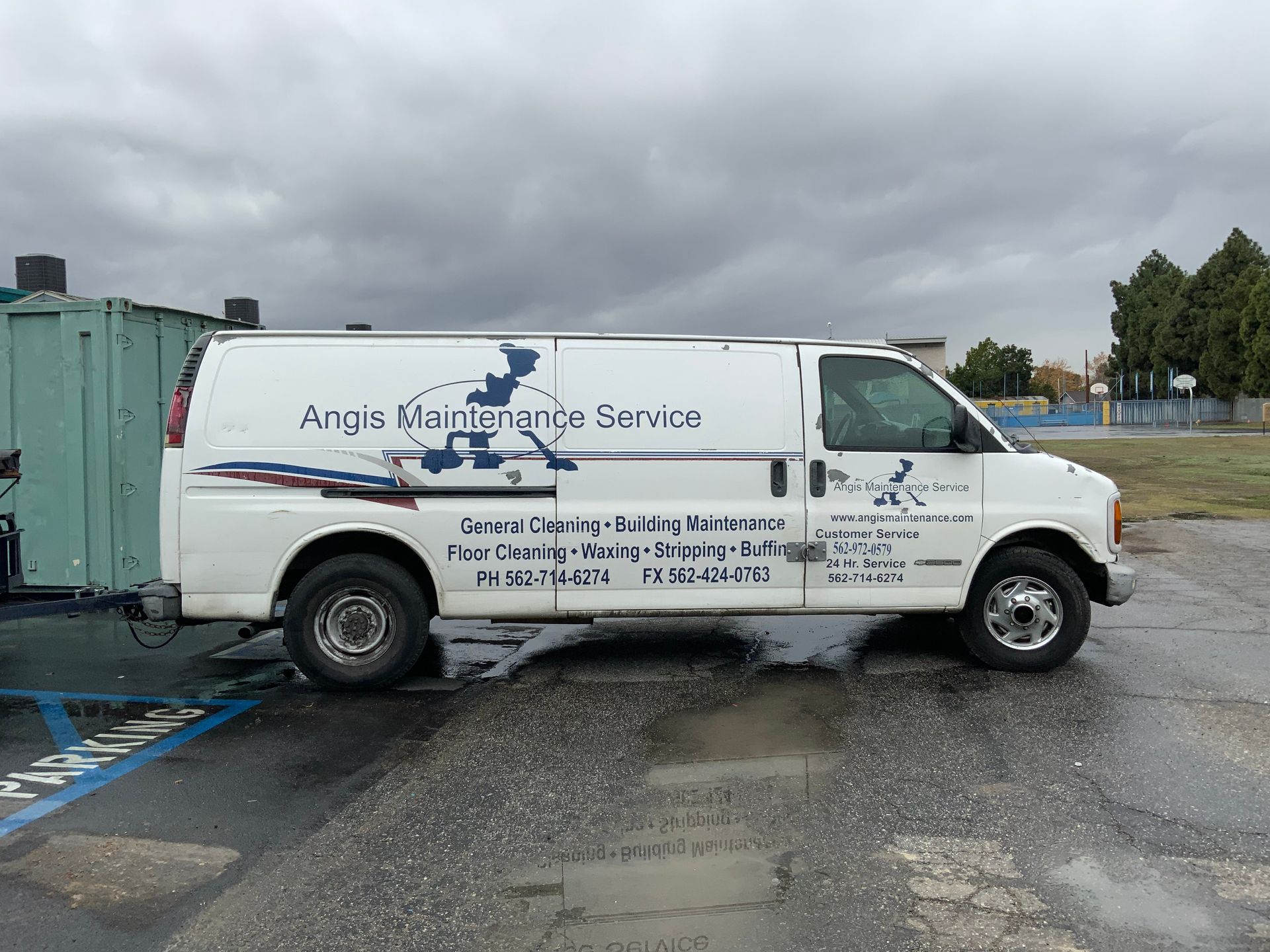 A white van is parked in a parking lot with a trailer attached to it.