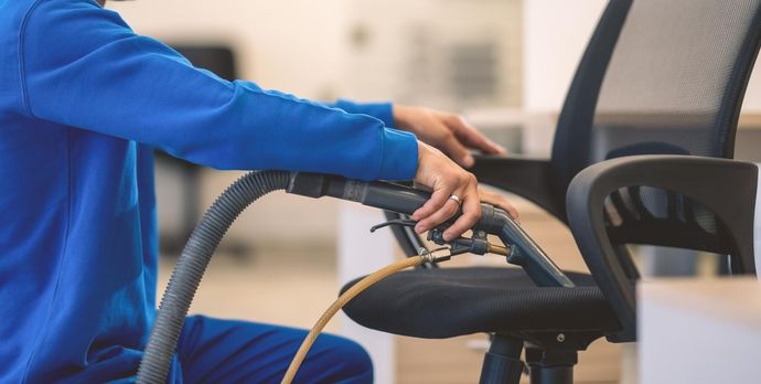 A man is cleaning an office chair with a vacuum cleaner.