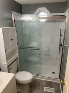 Bathroom with marble-look shower, white toilet, storage cabinet, and gray walls.