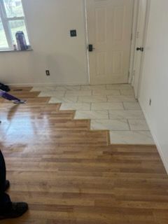 Wood and tile flooring transition in a room. A door is in the background.