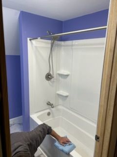 Bathroom with a person cleaning the white tub; purple walls.