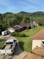 Truck parked in driveway in front of a house with a brown roof; green trees and hills in the background.