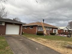 Brick house with attached garage, brown roof, and ladder leaning against it on a cloudy day.
