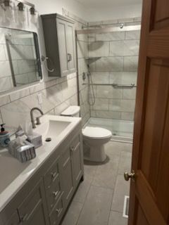 Bathroom with gray vanity, toilet, and shower with grab bar.