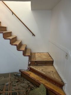 Staircase under construction with exposed wood steps and risers, handrail, and white walls.