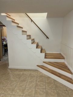 Wooden staircase with white risers and handrail in an interior setting. Brown tile flooring.
