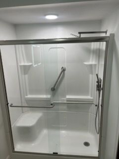 White accessible shower with glass doors, grab bars, and built-in seat.