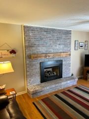 Fireplace with gray brick, wood mantel, and black firebox. A colorful rug is in front.