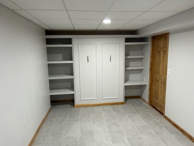 Built-in white cabinets with a fold-down bed in a room with a tiled floor and a wooden door.