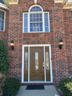 Red brick house with brown door, sidelights, and upper window. Two sconces flank the door.