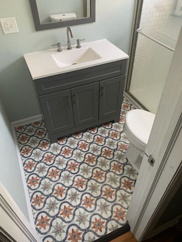 Bathroom with gray vanity, patterned floor tiles, white sink, toilet, and shower.