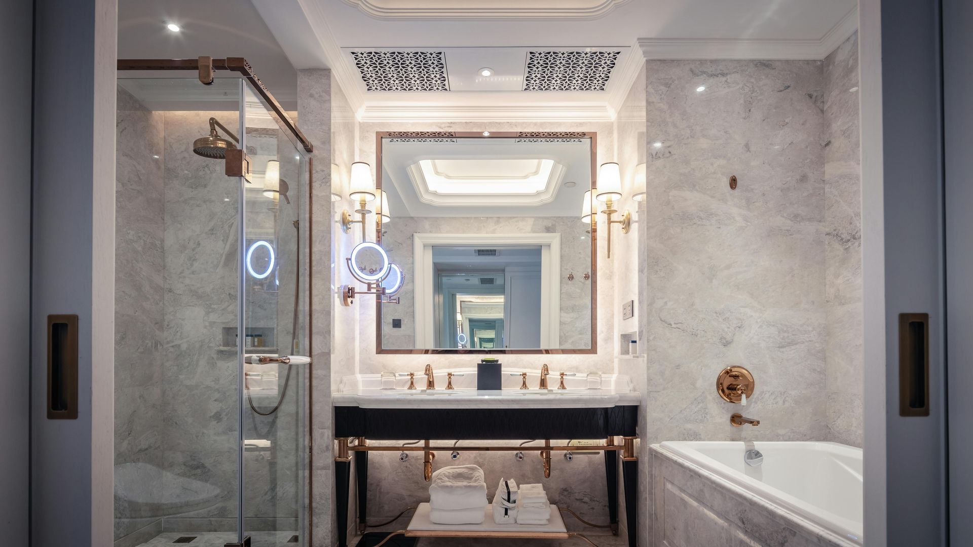 Luxurious bathroom with marble walls, double vanity, glass shower, and tub.
