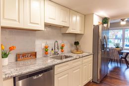 Cream-colored kitchen with granite countertops, stainless steel appliances, and a dining area in the background.
