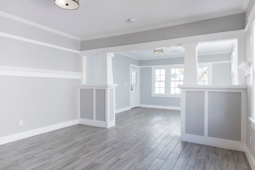 Empty room with gray wood-look flooring, light gray walls, white trim, and architectural details.