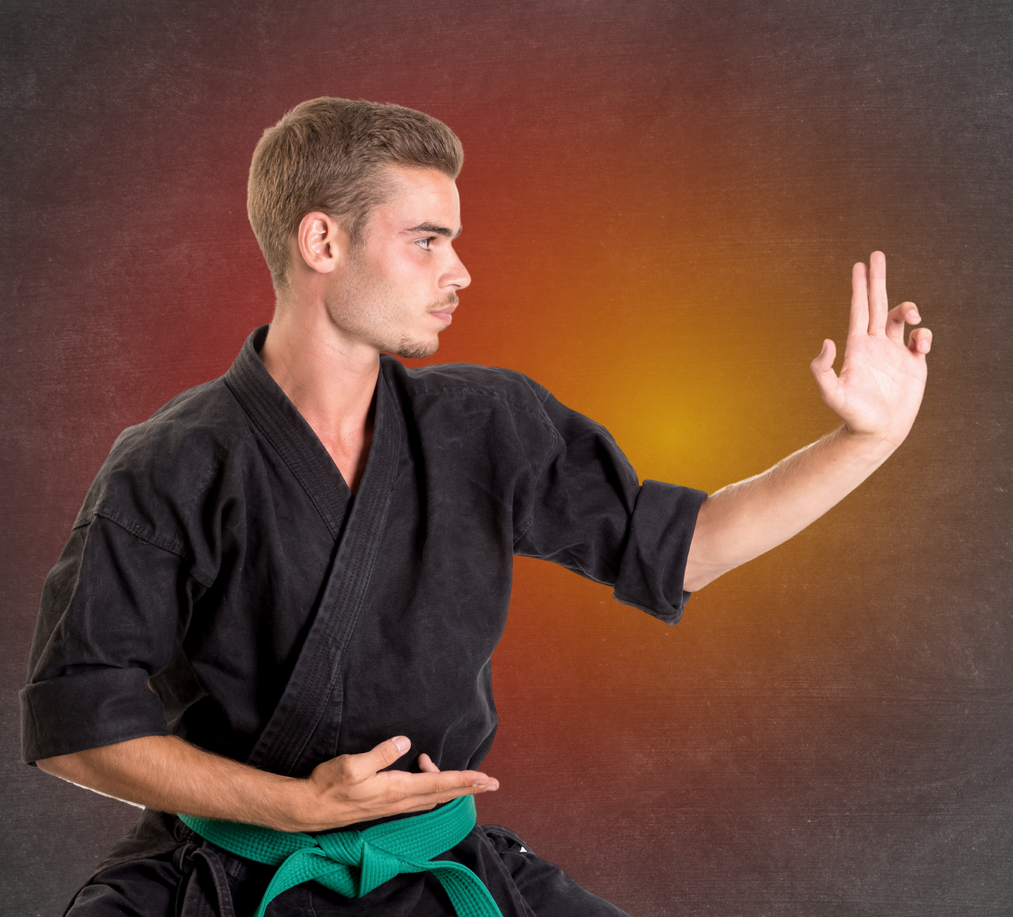 A young man in a black karate uniform with a green belt is practicing martial arts.
