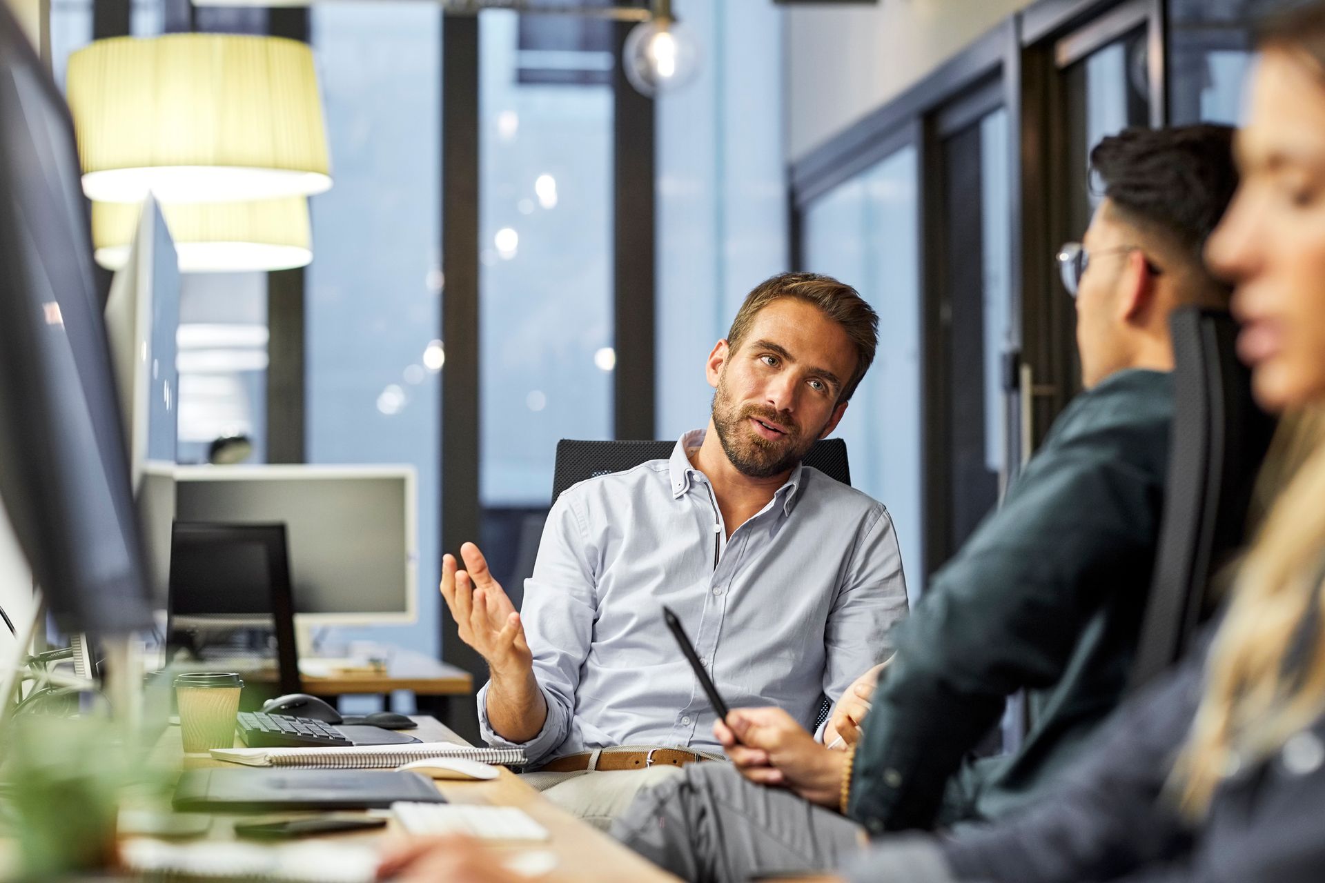 A man is sitting at a desk talking to a group of people in an office.