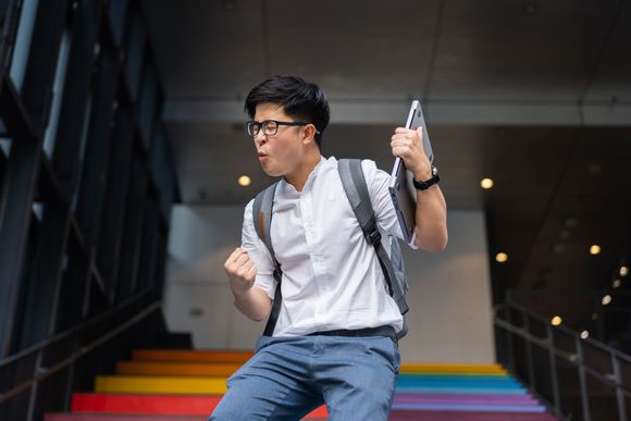 A man with a backpack is standing on a set of rainbow colored stairs.