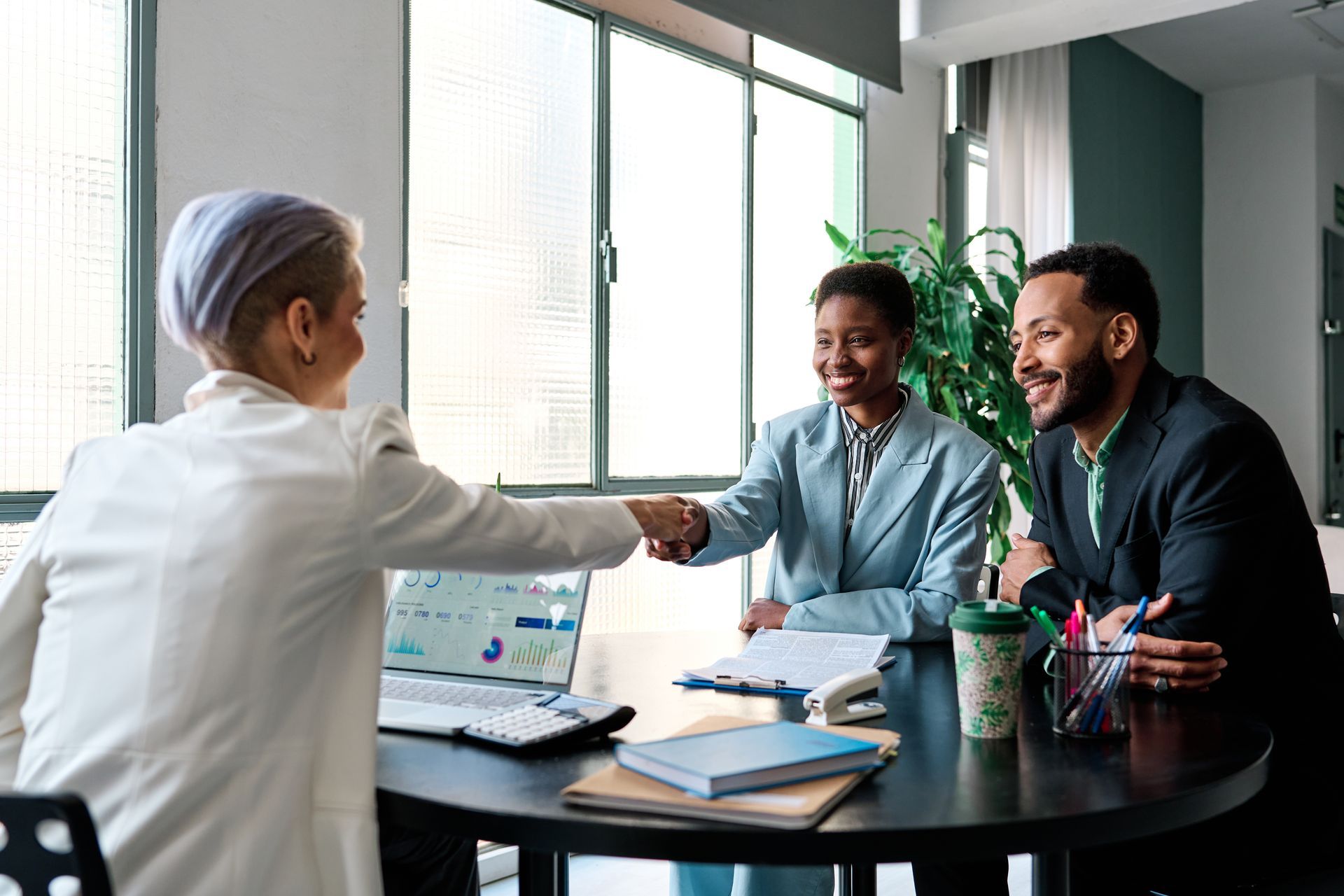 A woman is shaking hands with a man and a woman while sitting at a table.