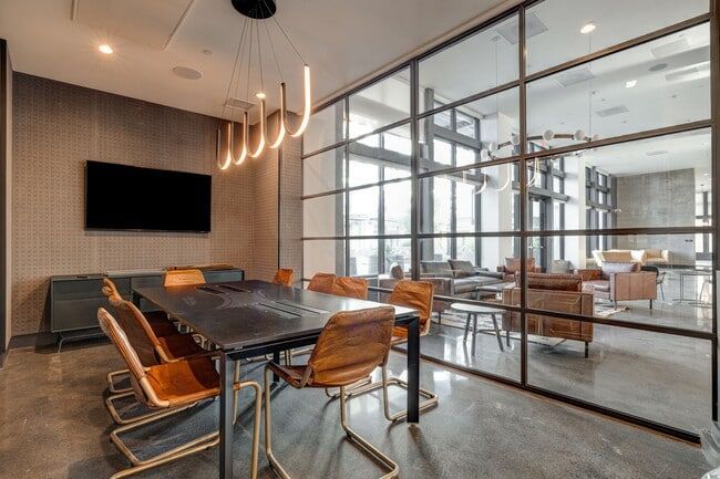 Meeting room with table and chairs, glass wall, and view into a lounge area.