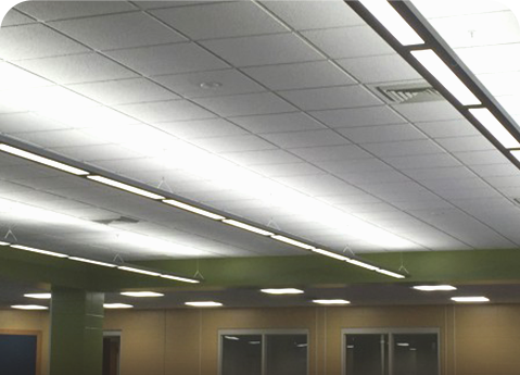 A drop ceiling featuring rows of long, bright fluorescent light fixtures, an air vent, and light green accent beams.