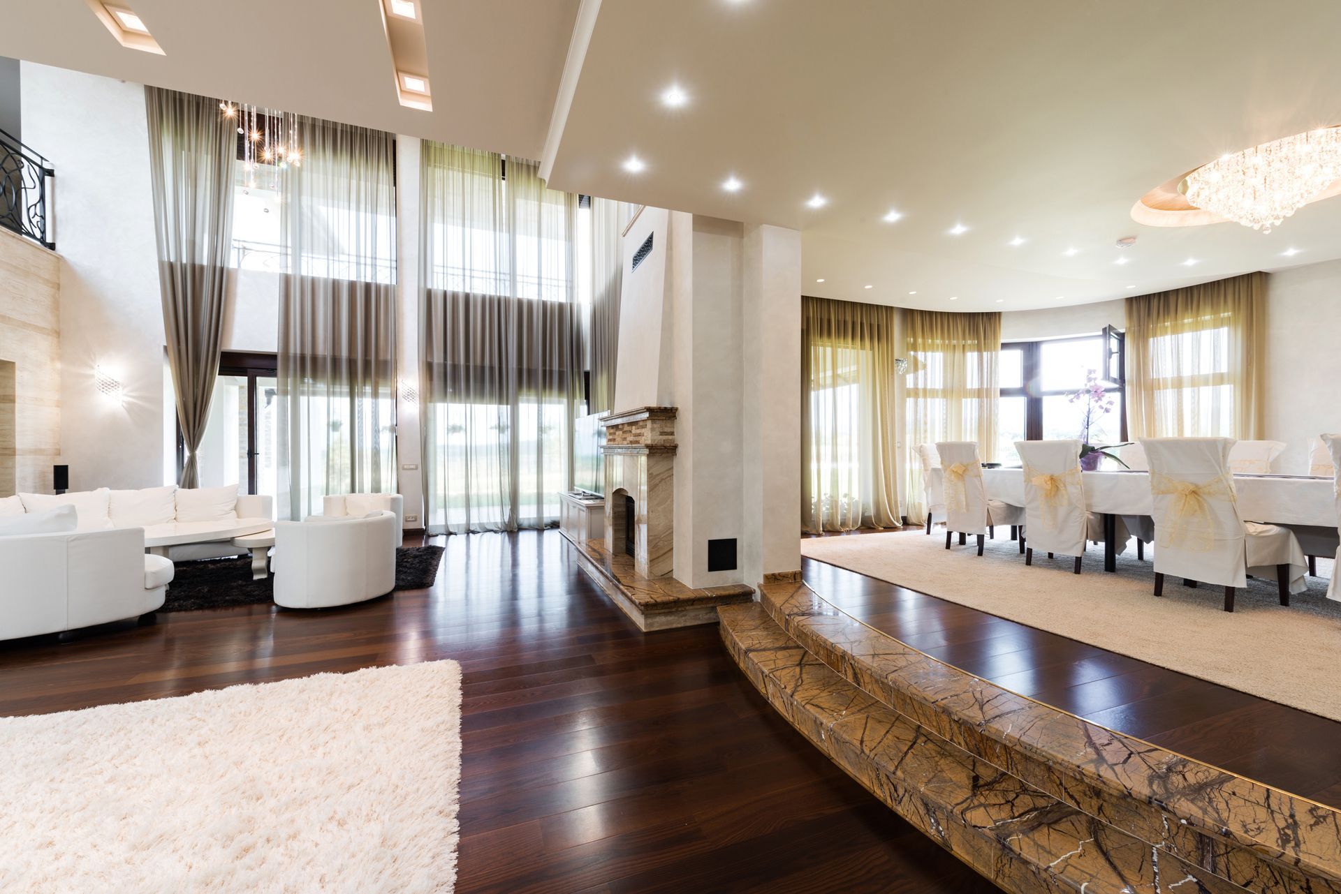 Spacious, modern living room with hardwood floors, a stone fireplace, and a dining area on a raised marble platform.