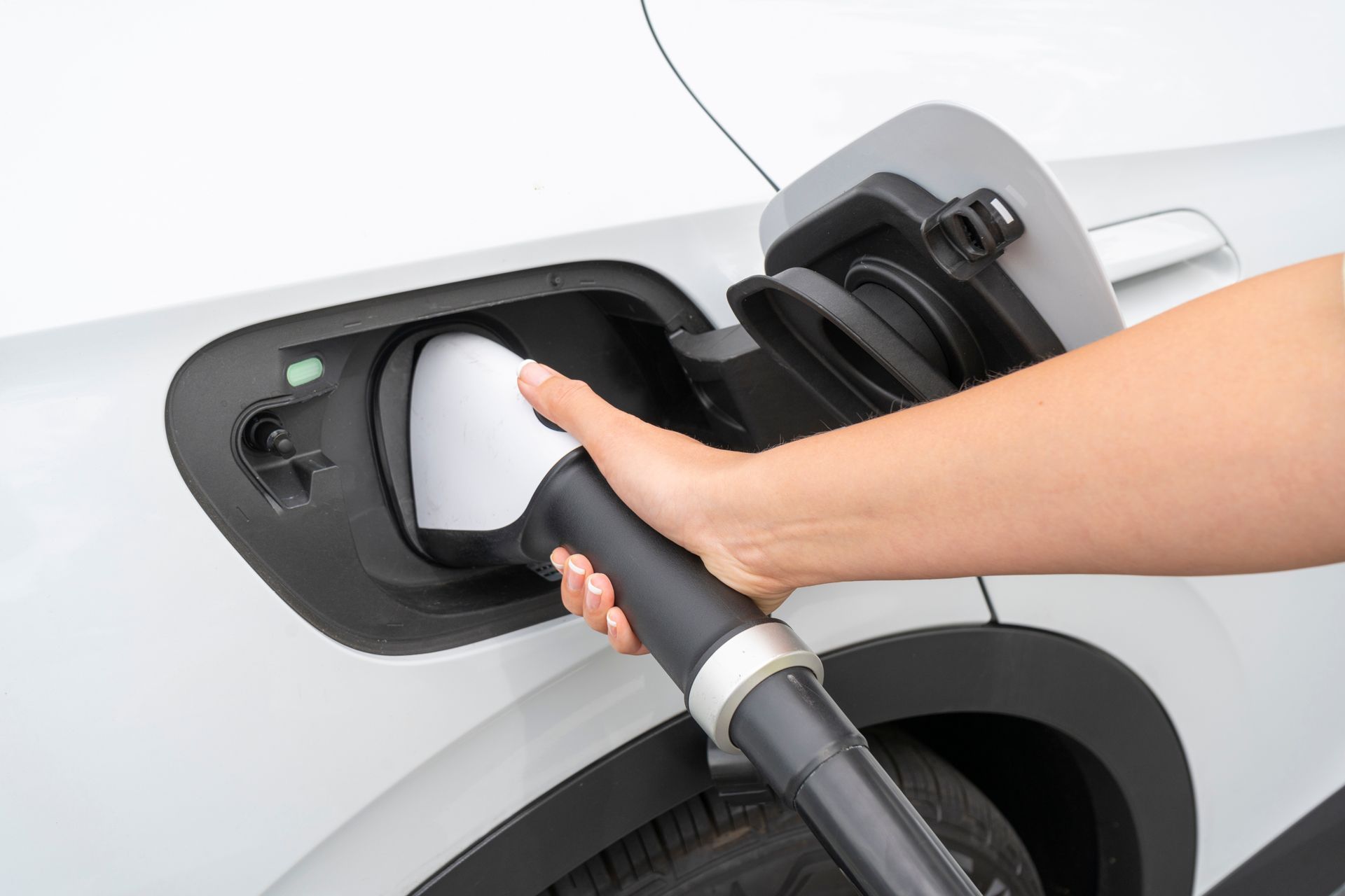 A hand plugging a charging cable into the port of a white electric vehicle.