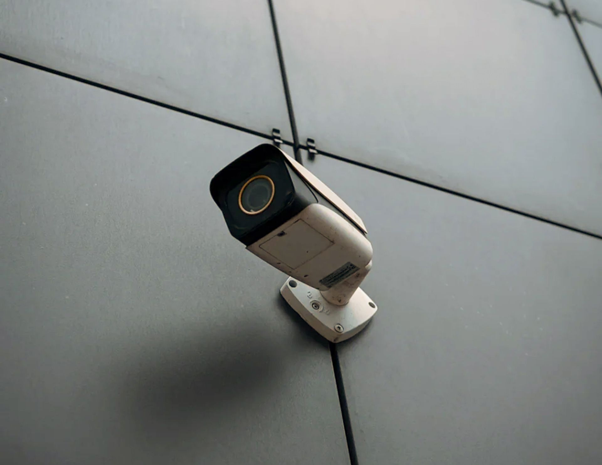 A white security camera mounted on a gray, tiled wall.