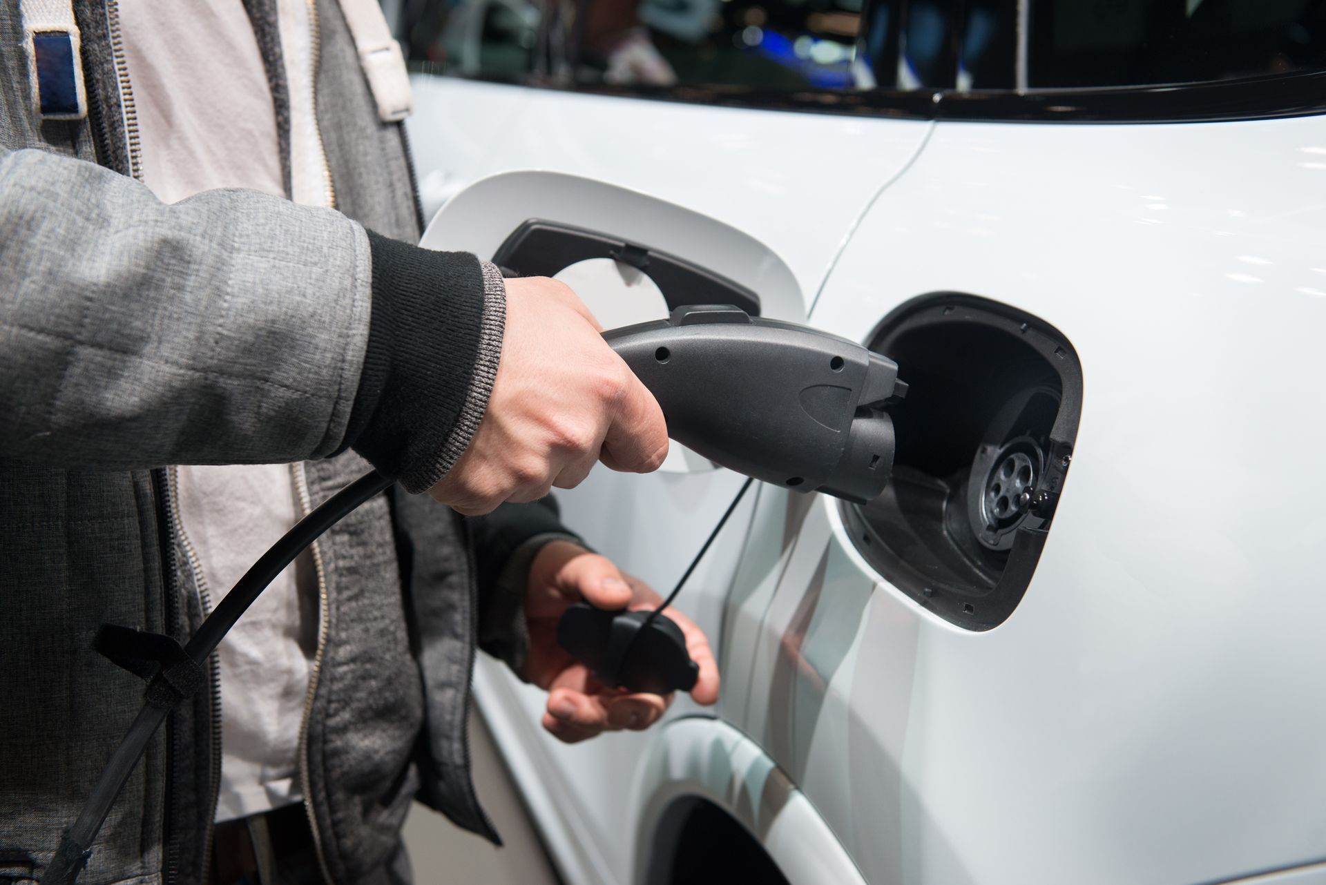 A person plugging a black electric vehicle charging cable into the charging port of a white car.