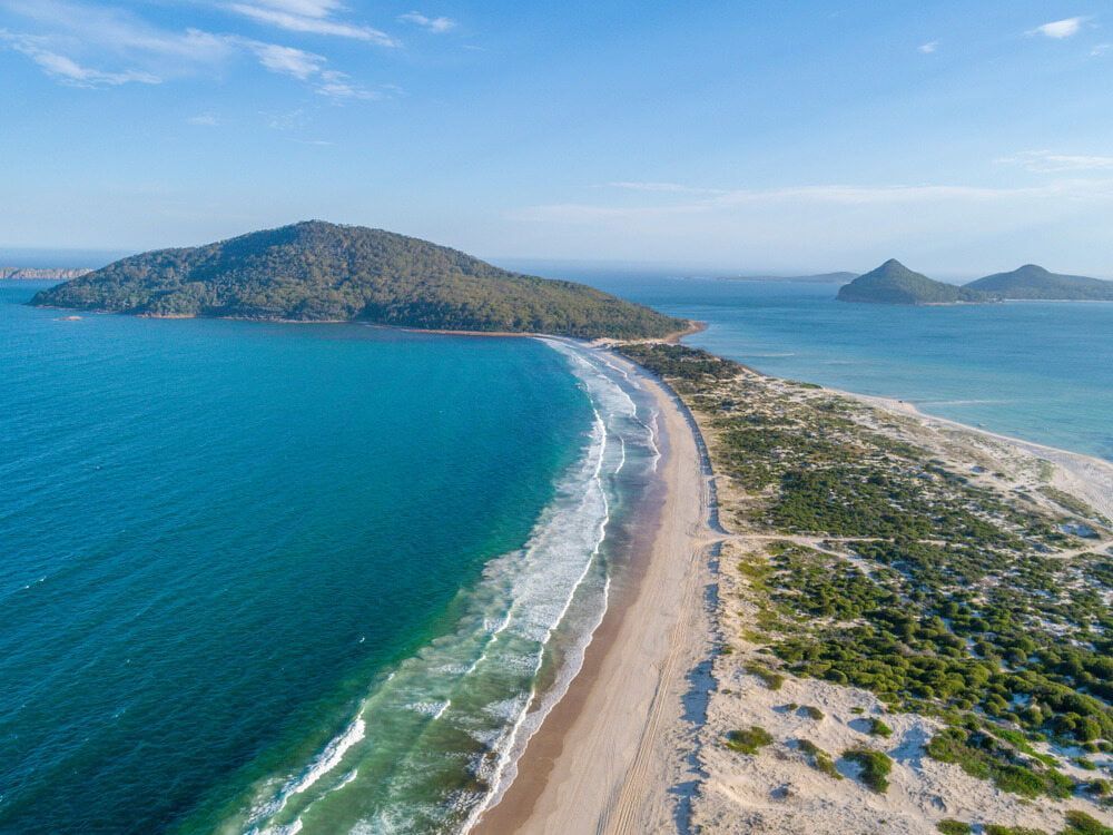 An Aerial View Of A Beach And Ocean With A Small Island In The Distance — The Kitchen & Bathroom Doctor in Hawks Nest, NSW