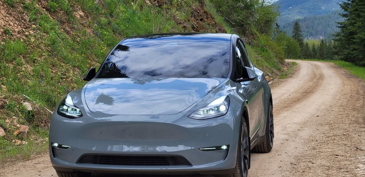 A tesla model y is driving down a dirt road.