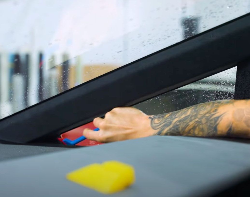 A man with a tattoo on his arm is cleaning the windshield of a car.