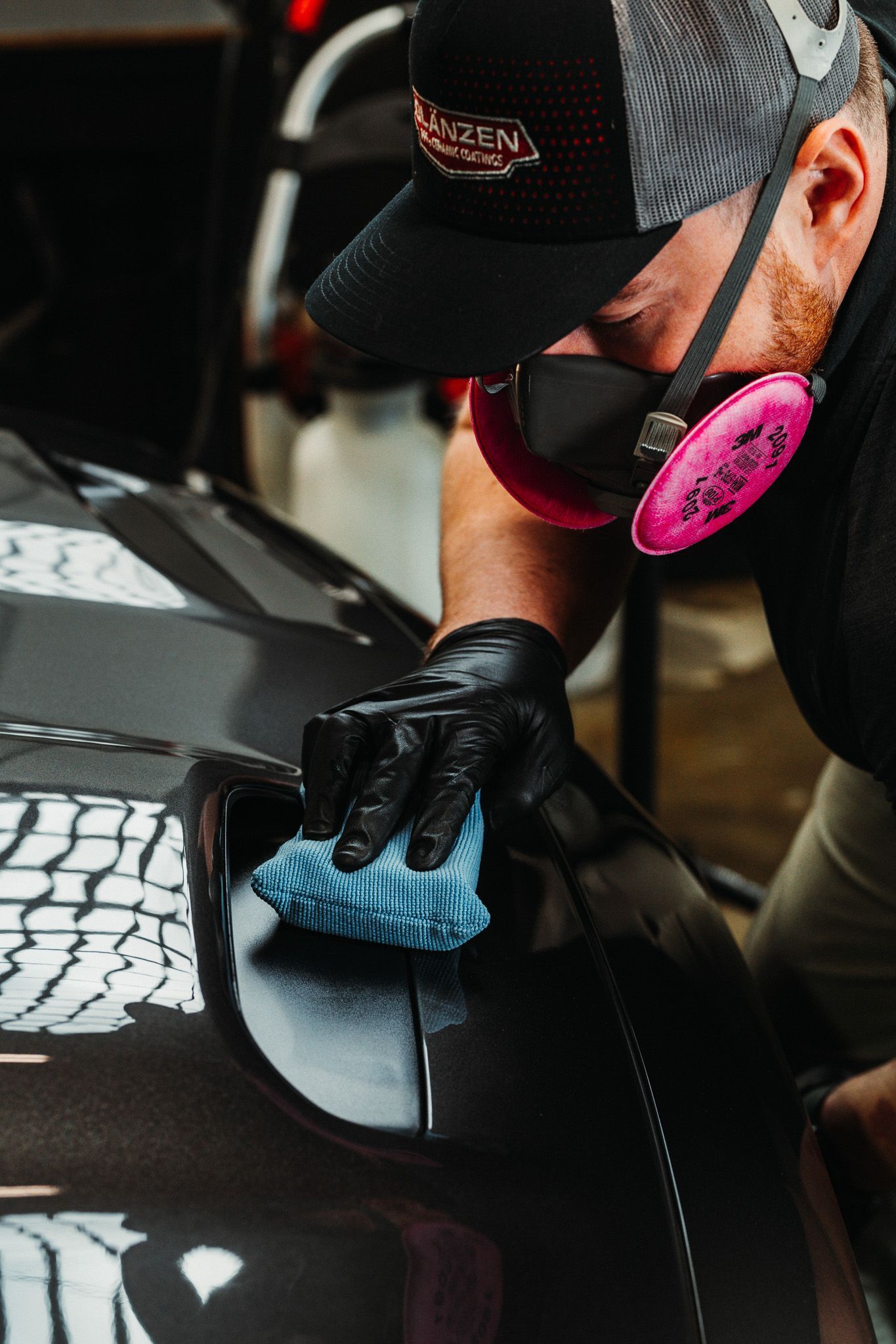 A man wearing a hat and gloves is cleaning a car with a cloth.