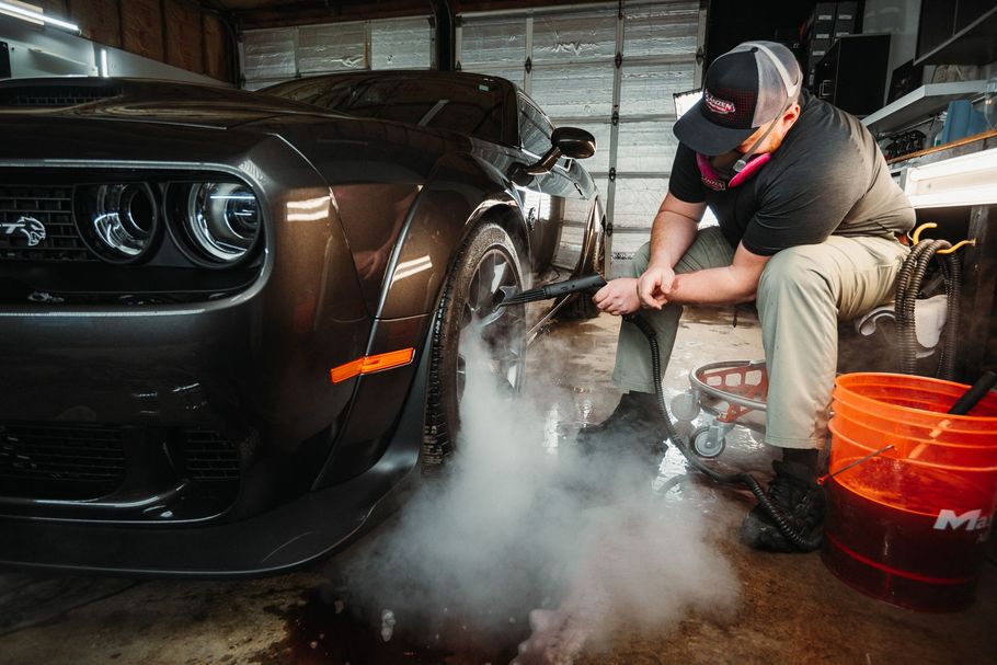 A man is cleaning the tires of a dodge challenger with a high pressure washer.