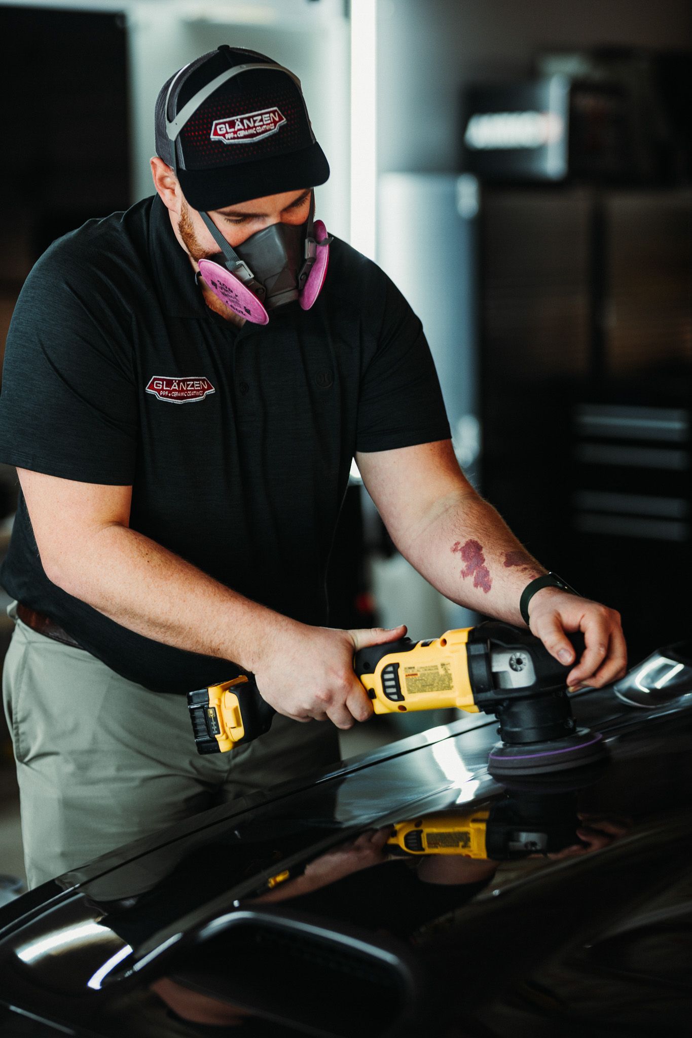 A man wearing a mask is polishing a car with a machine.