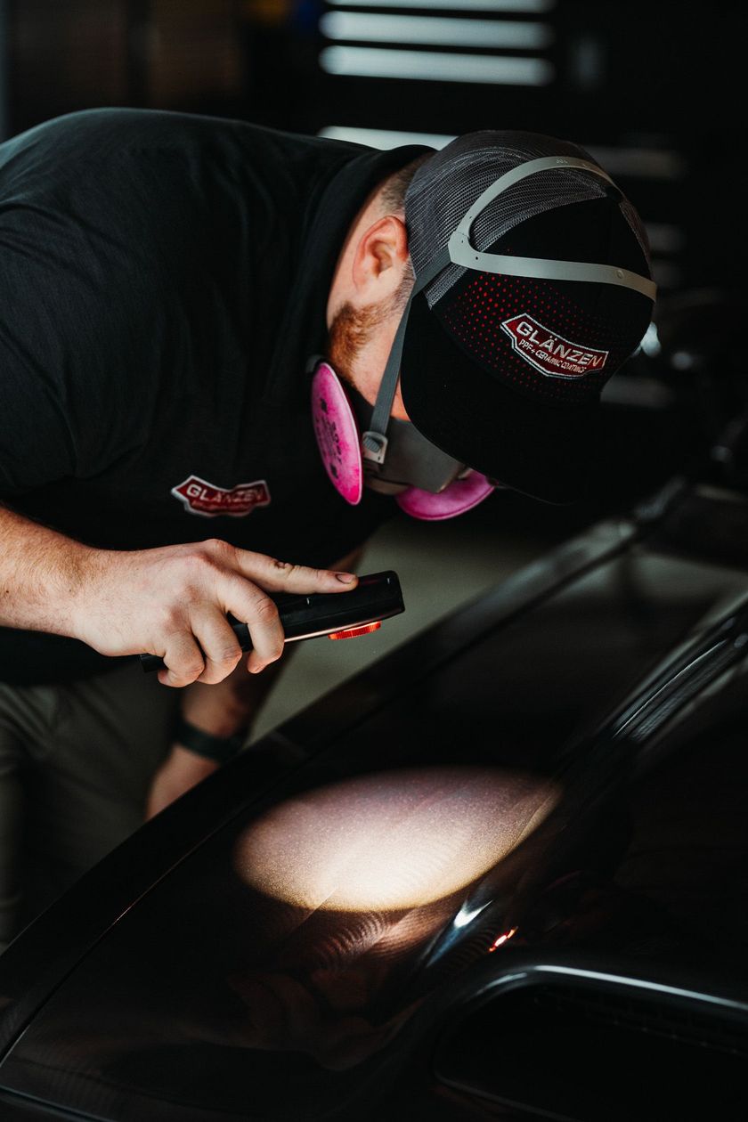 A man is looking under the hood of a car with a flashlight.
