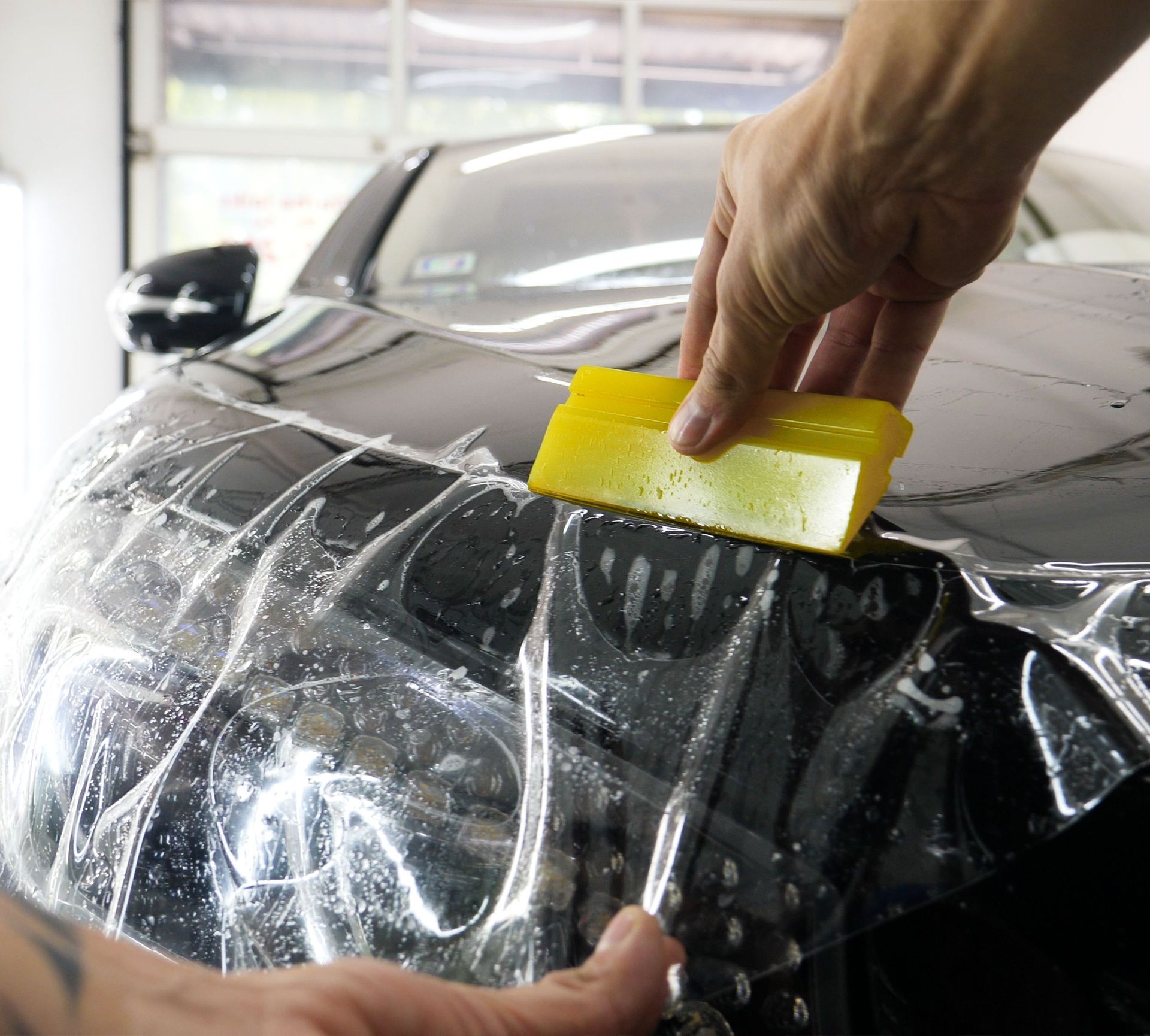 A person is wrapping a car with a yellow squeegee